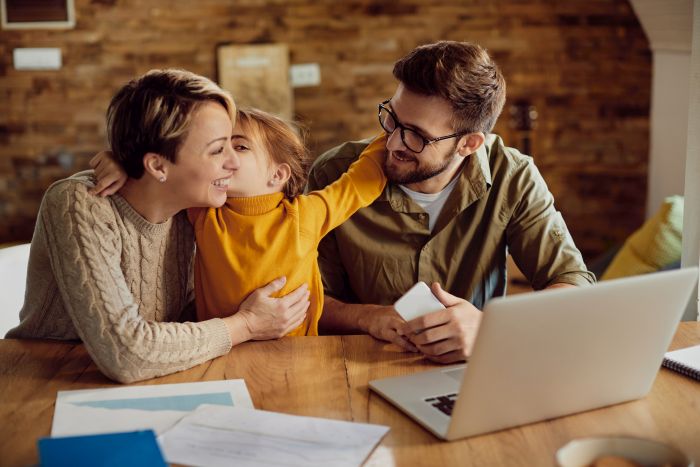 happy daughter embracing and kissing her working parents at home